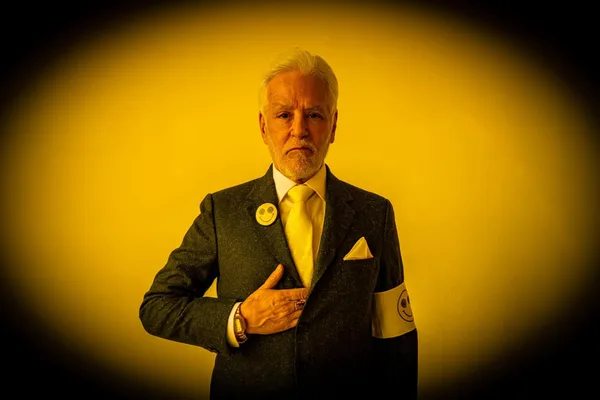 John Amedro in a dramatic yellow-lit portrait with smiley-face pins